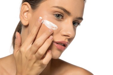 Güzel, genç, pozitif bir kadın beyaz bir stüdyo geçmişine yüz kremi sürüyor.