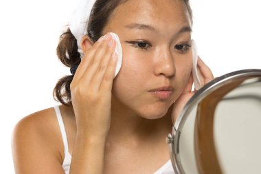 Güzel genç Asyalı kadın beyaz stüdyo arka planında pamuk pedlerle yüzünü temizliyor.