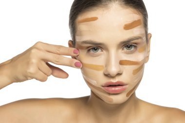 Güzel genç bir kadın parmaklarıyla farklı tonlarda sıvı fondöten sürüyor..