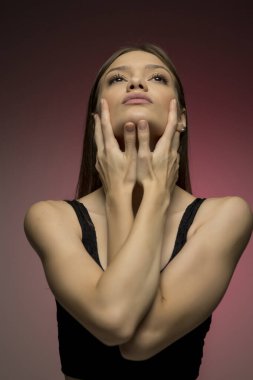 Elleriyle yüzünü çerçeveletmiş zarif poz veren genç bir kadının anlamlı bir görüntüsü. Öznenin zarafetini ve duygusal ifadesini vurgulayarak renkteki yumuşak geçişler.