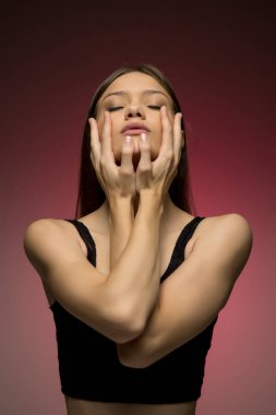 Elleriyle yüzünü çerçeveletmiş zarif poz veren genç bir kadının anlamlı bir görüntüsü. Öznenin zarafetini ve duygusal ifadesini vurgulayarak renkteki yumuşak geçişler.