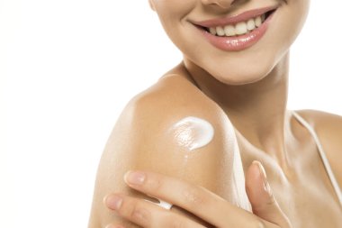 Işıl ışıl cilt, gülümseyen kadın, omuza sürülen beyaz krem, sergilenen su ve cilt bakımı.