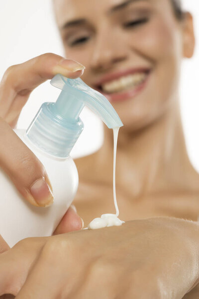 Close-up of a cheerful woman applying lotion from a pump dispenser, promoting skincare and wellness.