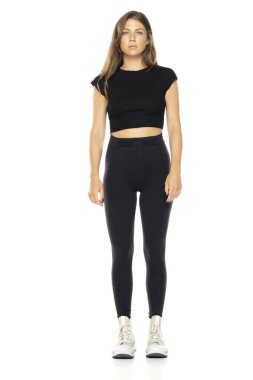 Siyah bluzlu ve yüksek bel taytlı genç bir kadın. Uzun kahverengi saçlı. Beyaz arka planda tam vücut çekimi. Beyaz spor ayakkabı giyiyordu. Tarafsız ifade.