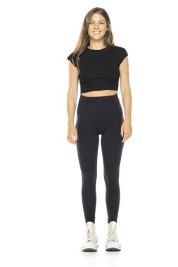 Siyah bluzlu ve yüksek bel taytlı gülümseyen genç bir kadın. Uzun kahverengi saçlı. Beyaz arka planda tam vücut çekimi. Beyaz spor ayakkabı giyiyordu. Tarafsız ifade.