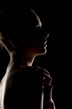 Profildeki dramatik kadın silueti. Gösterişsiz ışıklandırma hatları ve kıvrımları. Artistik çıplak fotoğraf konsepti ve minimum arkaplan.
