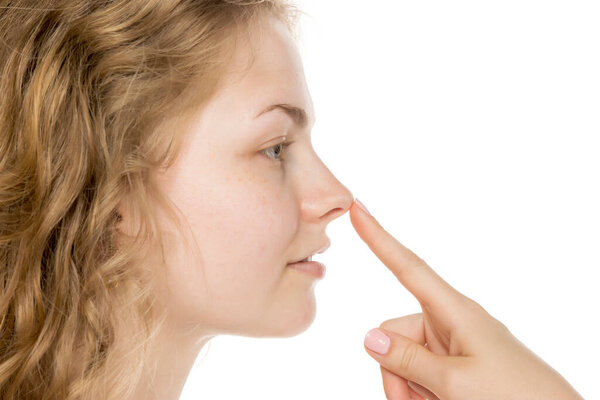 Close-up side view of young woman with curly blonde hair touching nose, suggesting nose job or plastic surgery concept. Isolated on white background, no makeup.