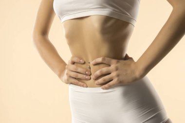 İnce gövdeli, beyaz iç çamaşırlı, elleri beline bastıran, zayıflatma efekti yaratan, bej arka plandaki tonlu mideyi ön plana çıkaran,