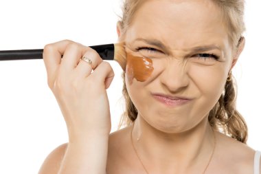 Cilt rengi için çok koyu olan temeli sıkarken yüzünü buruşturan genç bir kadın makyaj hatasından dolayı hayal kırıklığı yaşıyor..