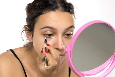 Makyaj fırçasıyla göz altına kapatıcı süren genç bir kadın. Güzellik rutinine yakın çekim, doğal görünüş. Asgari beyaz arkaplan ile stüdyo portresi.