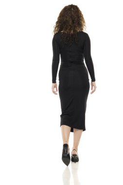 Kıvırcık esmer saçlı, uzun kollu siyah Midi elbisesi giyen, beyaz arka planda yürüyen, siluetini gösteren bir kadın..