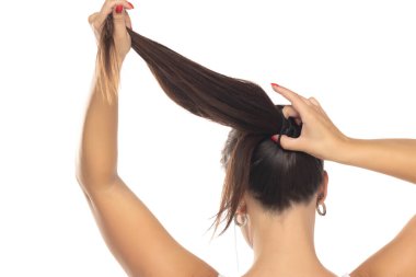 Uzun düz saçlarını at kuyruğuyla bağlayan, saçını yaptıran bir kadın. Saç bakım konsepti. Stüdyo çekimi, arka plan, beyaz stüdyo arka planda izole edilmiş.