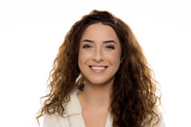Beyaz bornozlu, kıvırcık kahverengi saçlı kadın beyaz arka planda içten bir gülümseme, gerçek mutluluk, dostça bir ifade, doğal bir portre..