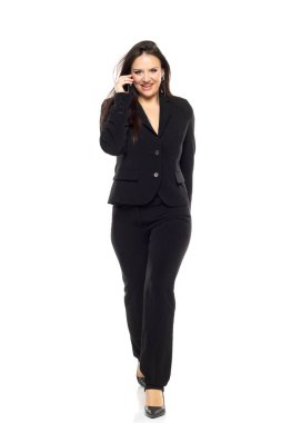 Gülümseyen iş kadını beyaz stüdyoda yürüyor ve cep telefonuyla konuşuyor. İş kavramı, kariyer gelişimi, hırslar, başarı, ofis yaşam tarzı