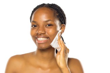 Siyah kadın ıslak mendille yüzünü temizlerken gülümsüyor, stüdyo resmi beyaz arka planda..