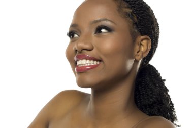 Makyajlı siyahi bir kadının beyaz arka planda gülümseyip bakışlarını kaçırdığı bir stüdyo resmi..