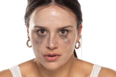 Beyaz bir stüdyo arka planında çıkarmadan önce yüz temizleme ürünüyle poz veren genç bir kadın.