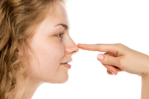 Close-up side view of young woman with curly blonde hair touching nose, suggesting nose job or plastic surgery concept. Isolated on white background, no makeup.