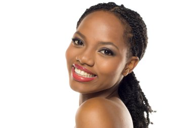 Makyajlı, beyaz arka planda gülümseyen ve başını eğen siyahi bir kadının stüdyo fotoğrafı..