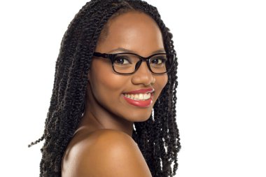 Saçları örgülü ve gözlüklü gülümseyen siyah bir kadın profilde poz veriyor, beyaz arka planda stüdyo çekimi.