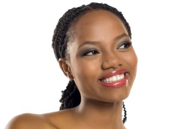 Makyajlı siyahi bir kadının beyaz arka planda gülümseyip bakışlarını kaçırdığı bir stüdyo resmi..