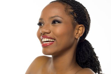 Makyajlı siyahi bir kadının beyaz arka planda gülümseyip bakışlarını kaçırdığı bir stüdyo resmi..