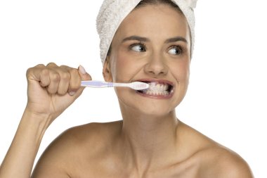 Dişlerini fırçalayan, yan bakan, hafifçe gülümseyen, beyaz arka planda çekim yapan genç bir kadın.