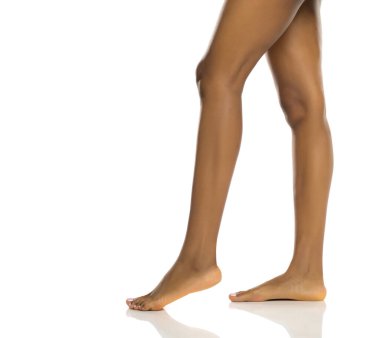 Hareket halindeki siyah bir kadının çıplak bacakları, kaldırılmış ayakla yan görüş, beyaz arka planda stüdyo çekimi.