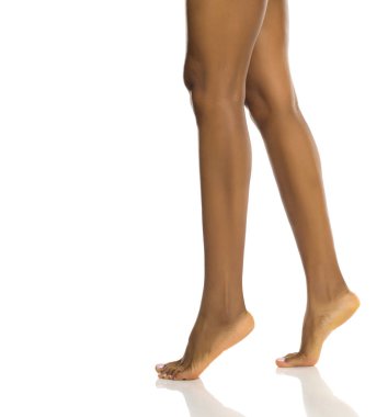 Parmak uçlarında yürüyen siyah bir kadının çıplak bacakları doğal hareket ve vücut dengesini gösteriyor, beyaz arka planda stüdyo çekimi var.