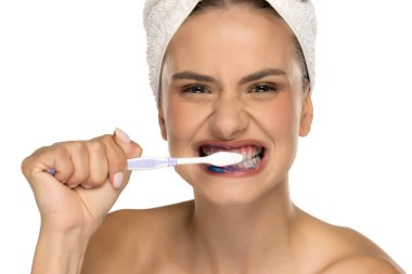 Mavi diş macunuyla dişlerini şiddetle fırçalayan genç bir kadın, beyaz arka planda stüdyo çekimi.