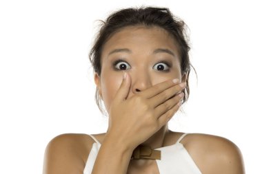 Beyaz arka plandaki stüdyo çekimlerinde, Asyalı kadının ağzını kapatan şok olmuş ifadesini görüyoruz.