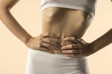 İnce gövdeli, beyaz iç çamaşırlı, elleri beline bastıran, zayıflatma efekti yaratan, bej arka plandaki tonlu mideyi ön plana çıkaran,