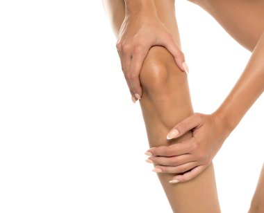 Beyaz arka planda dizini, vücut bakımını ve sağlık konseptini tutan kadınların el çekimi.