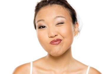 Makyajlı ve komik bir ifadeyle surat asan Asyalı kadın, beyaz arka planda stüdyo çekimi.