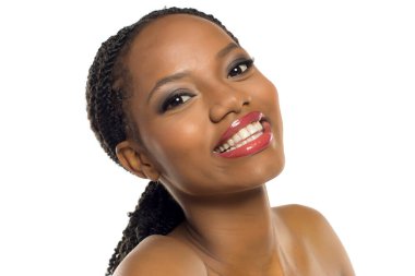 Makyajlı, beyaz arka planda gülümseyen ve başını eğen siyahi bir kadının stüdyo fotoğrafı..