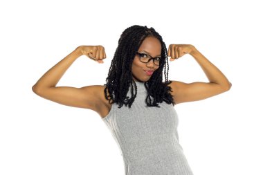 Gözlüklü, kendine güvenen siyah bir kadının beyaz arka planda çekimleri. İki kolunu da esnetiyor. Neşeli bir ifadeyle güç ve güç gösteriyor..