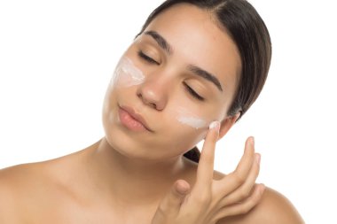 Kadın nazikçe yüz kremi sürüyor. Gözleri kapalı. Cilt bakımının tadını çıkarıyor.