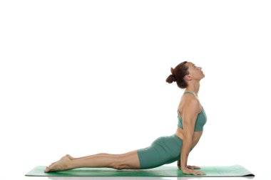 Yeşil elbiseli genç bir kadının beyaz arka planda yukarı doğru köpek yoga pozu (urdhva mukha svanasana) verirken çekilen fotoğrafı.