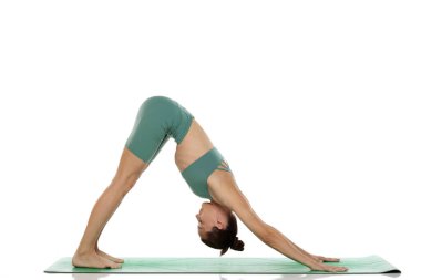 Yeşil elbiseli genç bir kadının beyaz arka planda köpek yoga pozu (adho mukha svanasana) verirken çekilen görüntüleri.