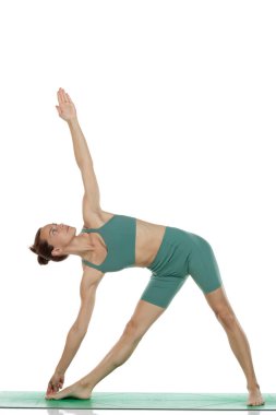 Beyaz arka planda yeşil kıyafetli genç bir kadının üçgen yoga pozu (trikonasana) verirken çekilmiş bir fotoğraf.