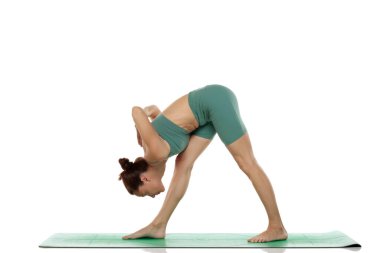 Yeşil elbiseli genç bir kadının beyaz arka planda piramit yoga pozu (parsvottanasana) verirken çekilmiş bir fotoğraf.