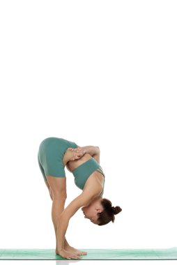 Yeşil elbiseli genç bir kadının beyaz arka planda yoga pozu (baddha uttanasana) verirken ki görüntüleri.