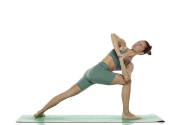 Yeşil elbiseli genç bir kadının beyaz arka planda dönen kenar açılı yoga pozu (parivrtta parsvakonasana) çekimleri.