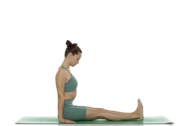 Yeşil elbiseli genç bir kadının beyaz arka planda yoga pozu (dandasana) verirken çekilmiş bir fotoğraf.