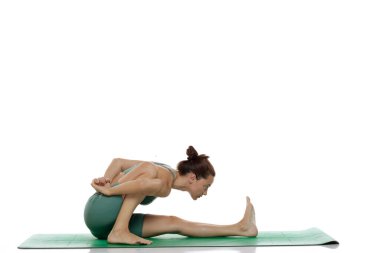 Beyaz arkaplanda baş-diz öne eğik yoga pozu (baddha janu sirsasana varyasyonu) pratiği yapan genç bir kadının stüdyo çekimi