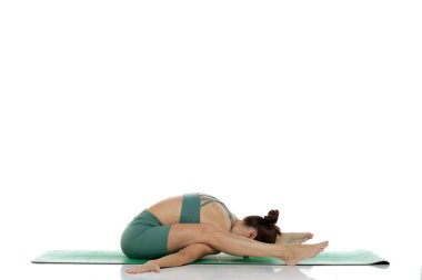 Yeşil elbiseli genç bir kadının beyaz arka planda kaplumbağa yoga pozu (kurmasana) çalışmasının stüdyo fotoğrafı.