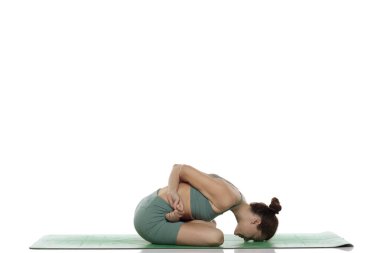 Yeşil elbiseli genç bir kadının stüdyoda çektiği fotoğraf, beyaz arka planda yoga pozisyonu (baddha balasana) veriyor..