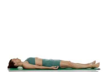 Yeşil elbiseli genç bir kadının, Savasana 'da uzanmış yoga pozu beyaz arka planda.