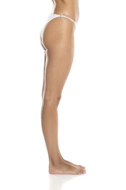 Beyaz bikinili alt gövde, beyaz arka planda yalınayak duran yan görüş.