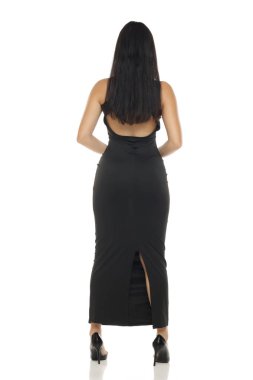 Sırtsız, siyah elbiseli, beyaz arka planda kameraya bakan esmer bir kadının stüdyo çekimi.